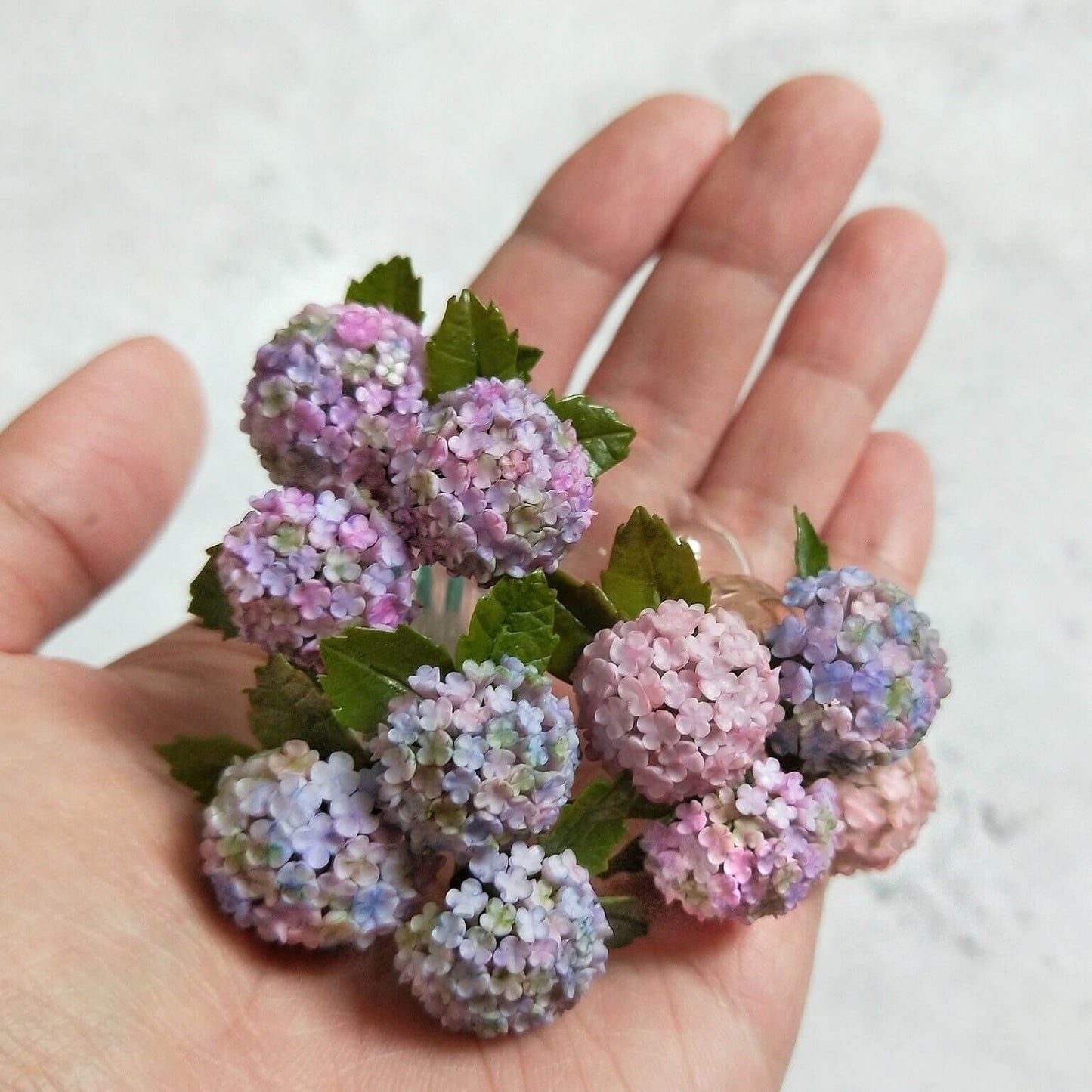 Hydrangeas are deciduous shrubs with flowers in terminal, round or umbrella-shaped clusters in colors of white, pink, or blue, or even purple. Scale: 1:6; 1:12 Material: Handmade from Clay Default Color: Random A variety of colors are available, choose your favorite color and make a note.