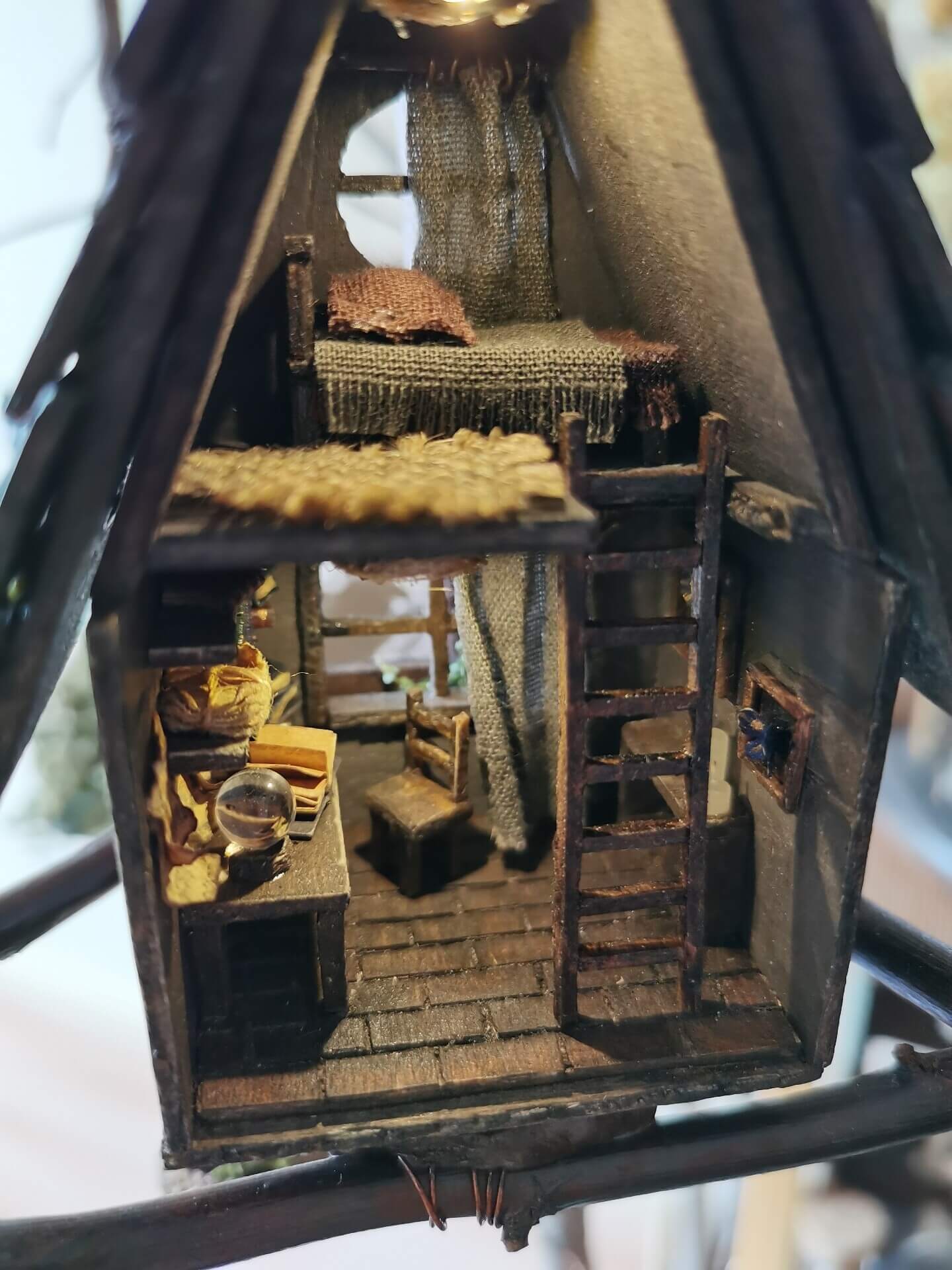 This miniature wooden treehouse exudes a whimsical, fairy-tale charm. It features a cozy loft bed under a slanted roof, accessible by a rustic wooden ladder. Warm lighting illuminates the intricate interior details, including a tiny desk, books, and woven fabrics, showcasing the delicate craftsmanship and magical ambiance of this enchanting creation.