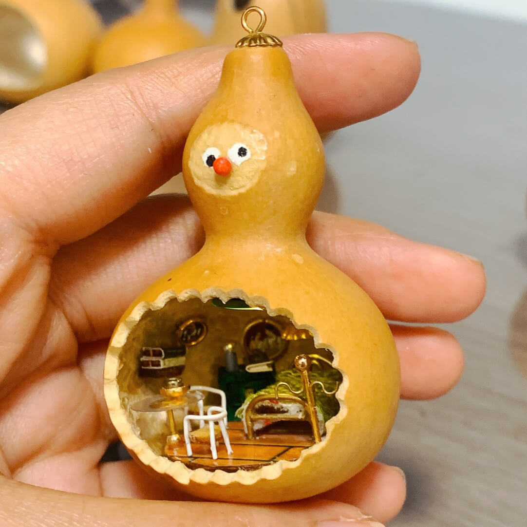 This adorable handcrafted gourd features a miniature bedroom tucked inside, complete with a cozy bed, a bedside table, and warm lighting. The intricate details, from the textured bedspread to the tiny furniture, create a whimsical and inviting space. Topped with a cheerful face, this gourd transforms into a charming piece of art that feels alive with personality and creativity.