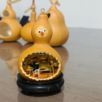 This adorable handcrafted gourd features a miniature bedroom tucked inside, complete with a cozy bed, a bedside table, and warm lighting. The intricate details, from the textured bedspread to the tiny furniture, create a whimsical and inviting space. Topped with a cheerful face, this gourd transforms into a charming piece of art that feels alive with personality and creativity.