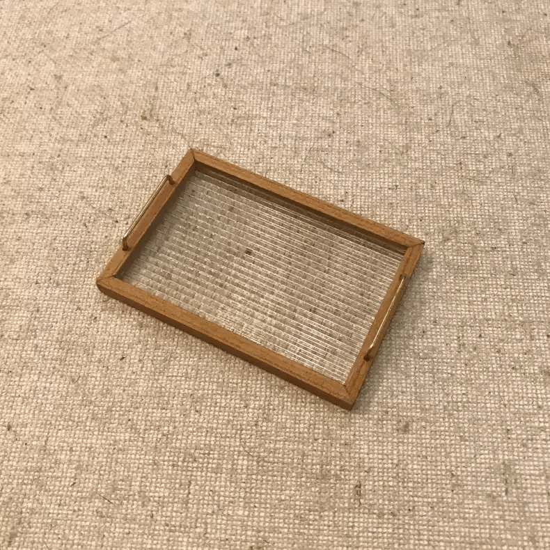 Add a charming and functional touch to your dollhouse with this Miniature Wooden Tray with Mesh Design. This elegantly crafted tray features a detailed mesh design, making it perfect for serving or displaying miniature items in your dollhouse. Its versatile and timeless style makes it a great addition to any miniature kitchen, dining room, or café setting.