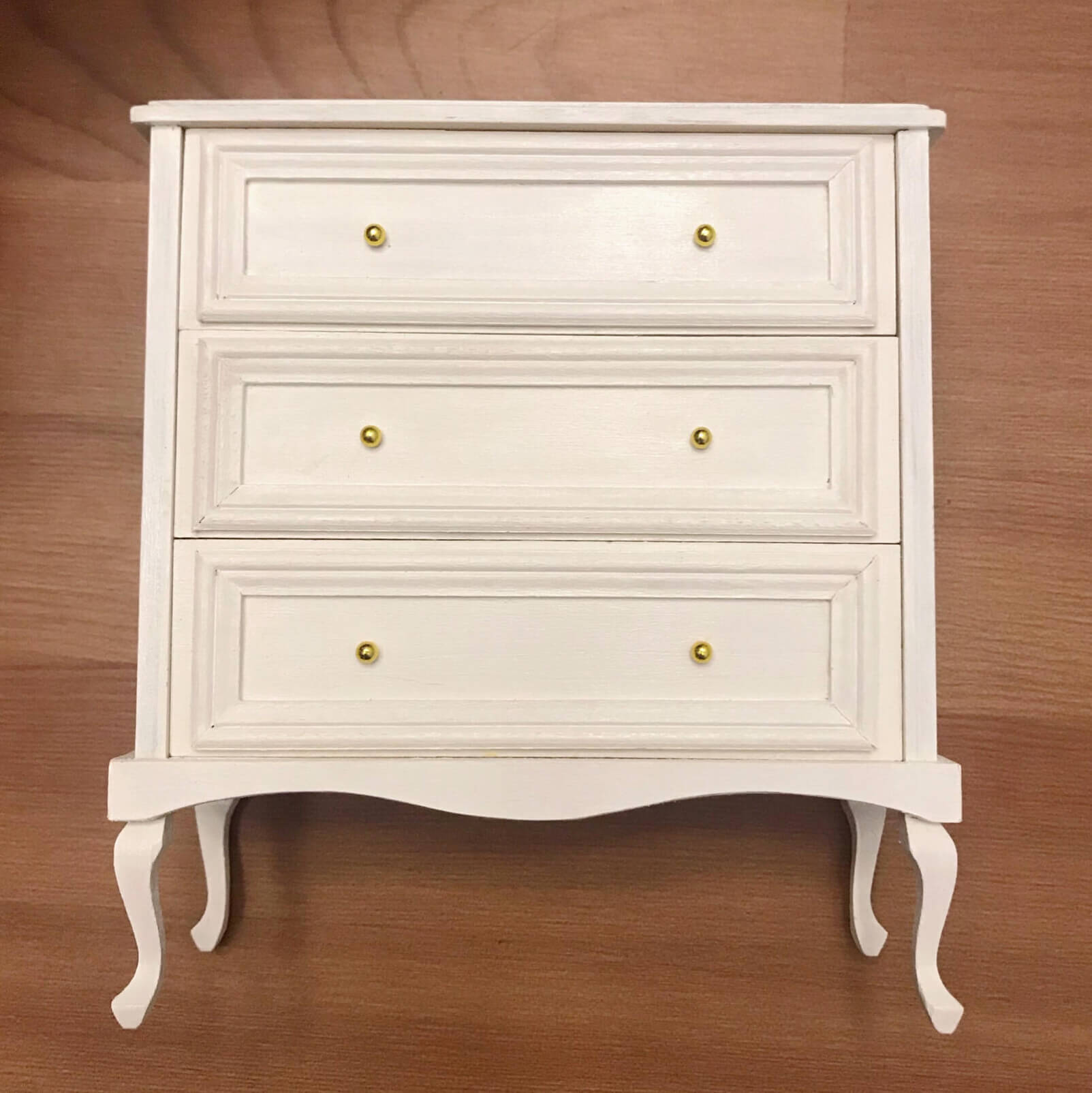 It boasts three spacious drawers, providing ample storage for your essentials. Supported by graceful cabriole legs, this dollhouse chest of drawers combines classic French design with functional elegance, making it a perfect addition to any dollhouse bedroom or living area seeking a touch of refined style and historical charm.