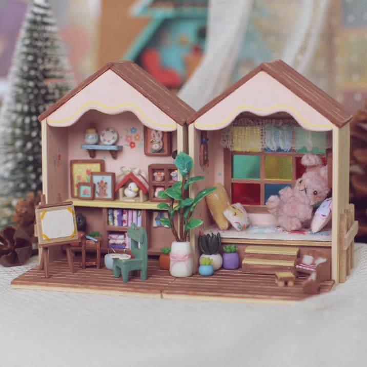 This foldable miniature dollhouse opens up to reveal two charming rooms filled with detailed, removable furniture. One side features an artistic studio with a cozy easel, plant decor, and a workspace, while the other side offers a relaxing bedroom with colorful pillows, a plush bed, and a vibrant window. Each piece, from the tiny bookshelves to the small plants, is meticulously crafted, making it an ideal addition for collectors or anyone who loves unique, interactive designs.