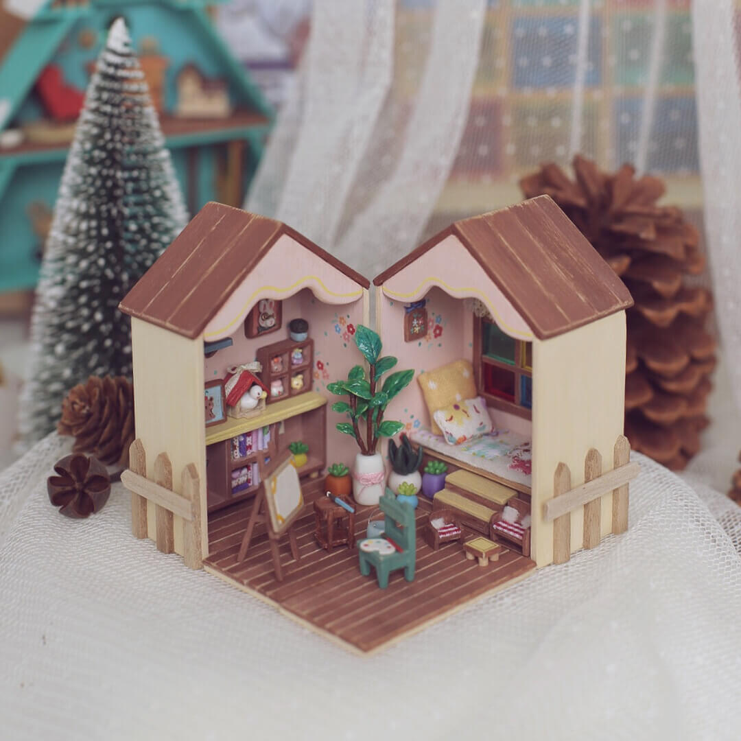 This foldable miniature dollhouse opens up to reveal two charming rooms filled with detailed, removable furniture. One side features an artistic studio with a cozy easel, plant decor, and a workspace, while the other side offers a relaxing bedroom with colorful pillows, a plush bed, and a vibrant window. Each piece, from the tiny bookshelves to the small plants, is meticulously crafted, making it an ideal addition for collectors or anyone who loves unique, interactive designs.