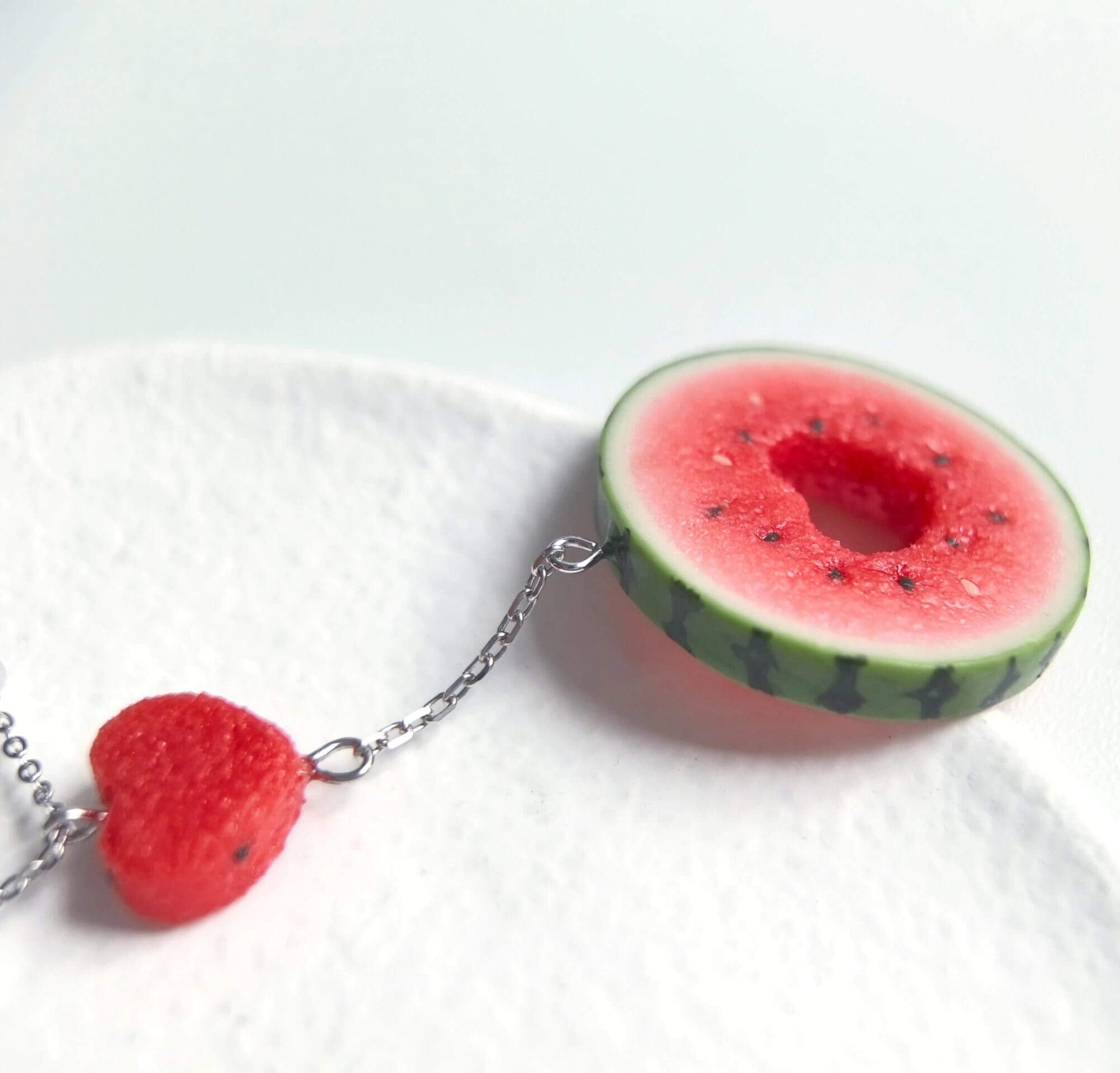 Cute realistic round watermelon slice with cut in the shape of heart necklace with sterling silver chain. The watermelon are made with polymer clay and then finished with a gloss varnish. The necklace are made from high-quality materials and are durable, but should not be put in aggressive environments like excessive moisture, chemicals or perfume.