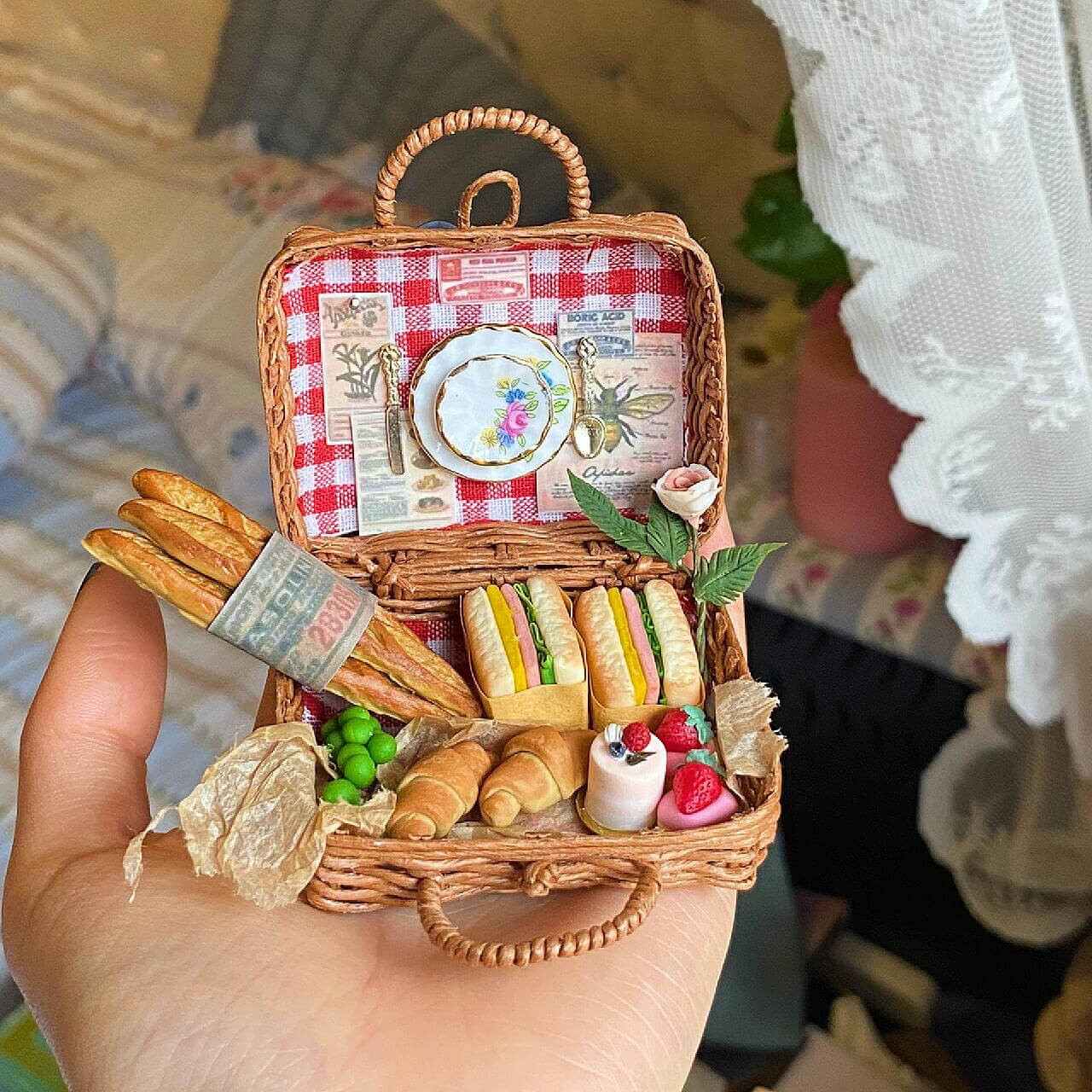 This charming miniature picnic basket brings the essence of a French picnic to life. With a red checkered lining, it features mini baguettes, sandwiches, croissants, peas, and strawberries. A delicate porcelain plate and cutlery add a touch of elegance, while intricate paper details and a tiny rose complete the idyllic scene. Perfectly crafted, it's a delightful escape into the art of miniatures!