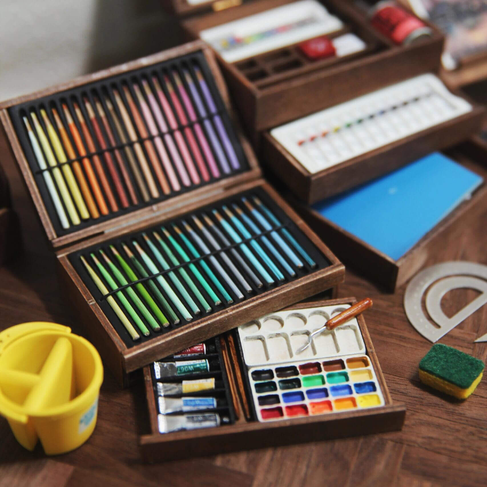 This unpainted miniature artist's paint box kit with pencils, palette and watercolor tubes is designed for dollhouse enthusiasts who enjoy custom crafting. The kit includes unpainted wooden pencils and watercolor tubes, along with a detailed, unpainted palette, all neatly organized in miniature wooden boxes.