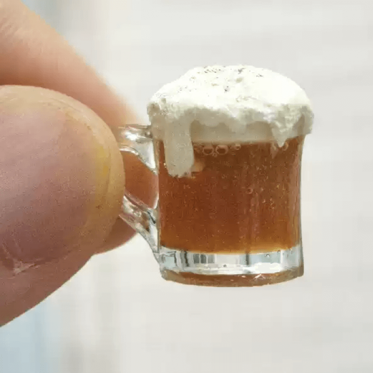 A miniature mug filled with pale beer or ale with a nice head of foam on top. The perfect drink for your dolls.