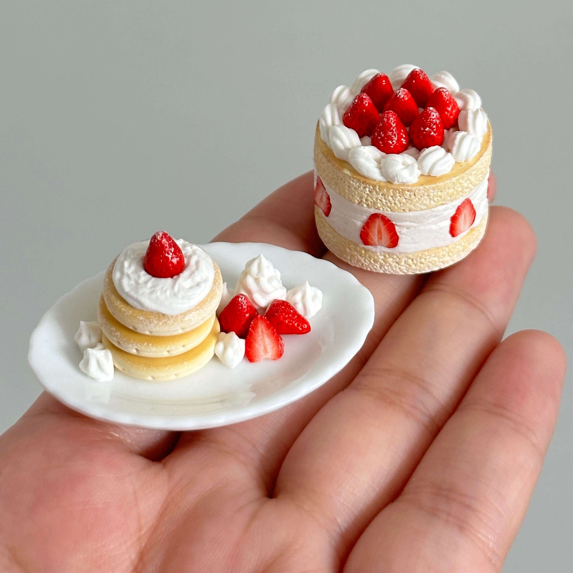 This charming miniature dessert display case is a sweet-tooth's dream brought to life. Featuring perfectly detailed strawberry shortcakes and pancake, each creation looks as delectable as the real thing. The rustic white display cabinet adds a cozy bakery vibe, enhancing the charm of these handcrafted treats. Every element, from the whipped cream to the vibrant strawberries, showcases the meticulous artistry and attention to detail.