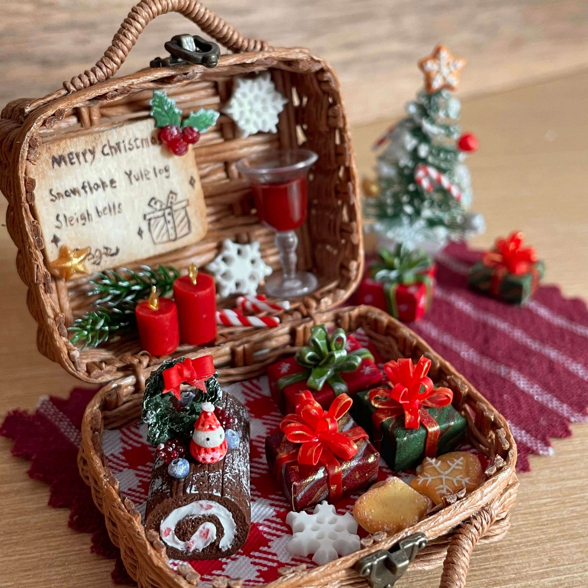 This festive miniature basket captures the magic of Christmas with incredible detail. Inside, you'll find tiny wrapped gifts, a cake, red candles, and a glass of wine, all arranged on a checkered cloth. The scene is complete with a mini Christmas tree and joyful holiday decorations, creating a cozy and enchanting holiday atmosphere.