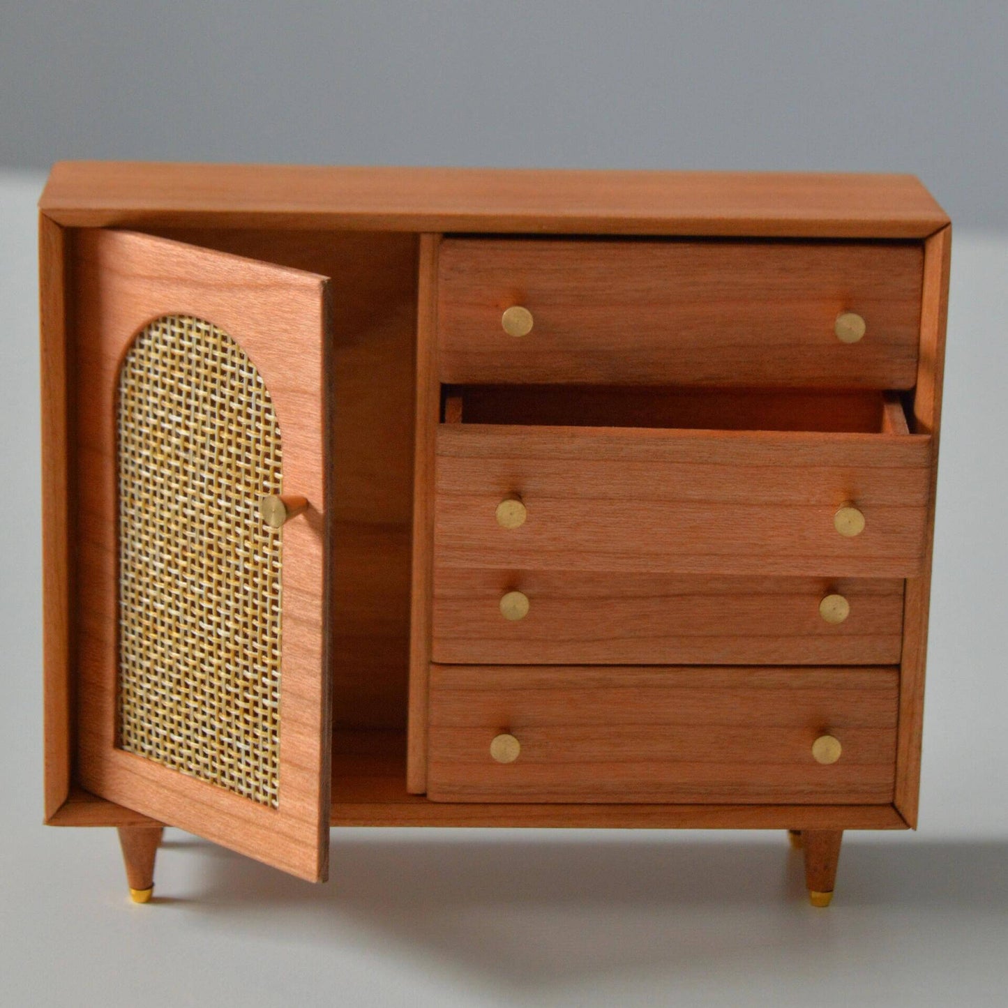 Add a touch of elegance and charm to your dollhouse with this Miniature Wooden Storage Cabinet with Faux Rattan Door and Drawers Kit. The cabinet features a stylish faux rattan design on the door, combined with sleek wooden drawers that provide practical storage. The beautiful finish and classic handles add sophistication to this piece, making it a perfect addition to any miniature living room, bedroom, or office.