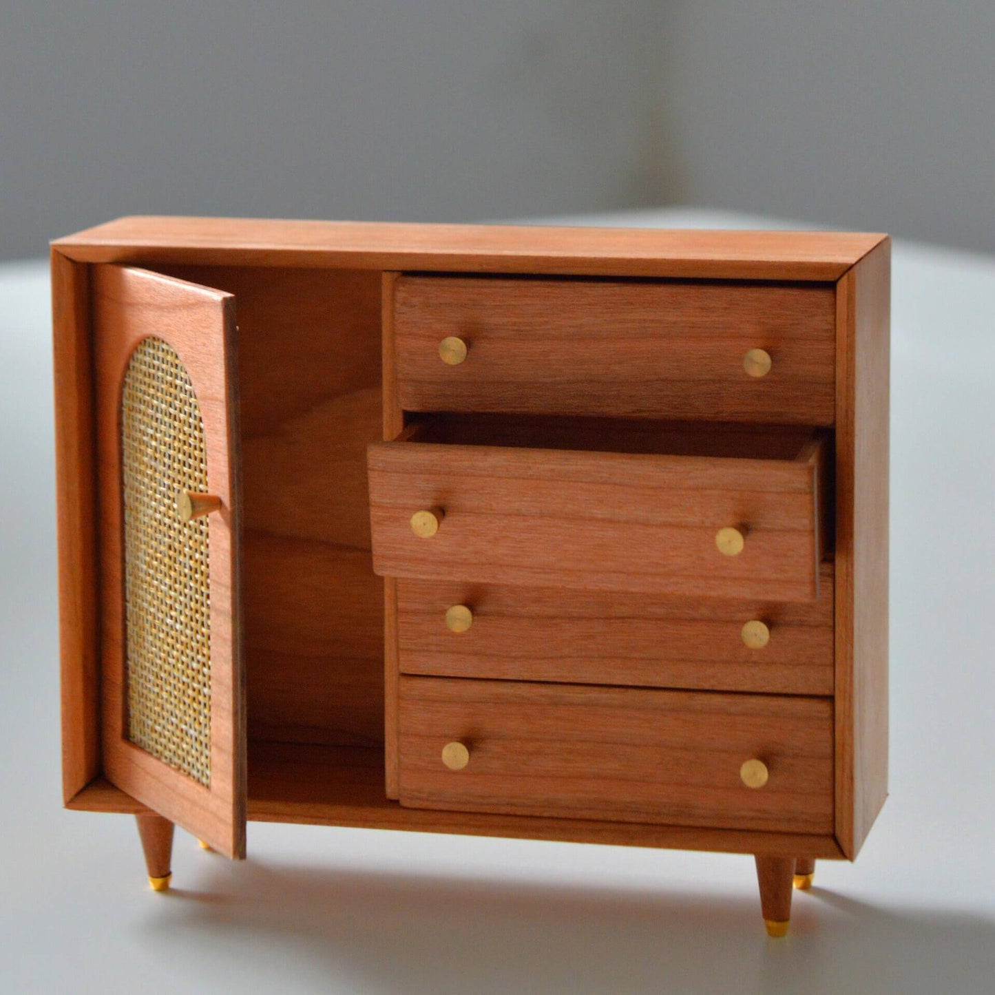 Add a touch of elegance and charm to your dollhouse with this Miniature Wooden Storage Cabinet with Faux Rattan Door and Drawers Kit. The cabinet features a stylish faux rattan design on the door, combined with sleek wooden drawers that provide practical storage. The beautiful finish and classic handles add sophistication to this piece, making it a perfect addition to any miniature living room, bedroom, or office.