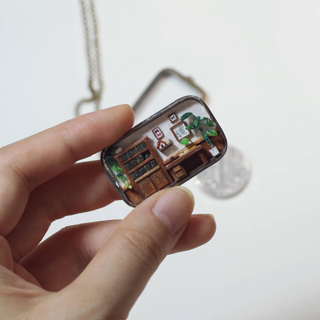 This is a delicate miniature pendant featuring a tiny study room. Inside the pendant’s frame lies a meticulously crafted scene, complete with a wooden desk, bookshelf, potted plants, and tiny decorations, evoking the warmth and charm of a cozy workspace. Perfect as both jewelry and an art piece, it combines creativity and craftsmanship in an enchanting way.