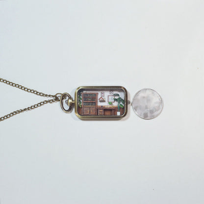 This is a delicate miniature pendant featuring a tiny study room. Inside the pendant’s frame lies a meticulously crafted scene, complete with a wooden desk, bookshelf, potted plants, and tiny decorations, evoking the warmth and charm of a cozy workspace. Perfect as both jewelry and an art piece, it combines creativity and craftsmanship in an enchanting way.