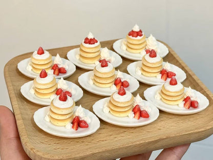 This charming miniature dessert display case is a sweet-tooth's dream brought to life. Featuring perfectly detailed strawberry shortcakes and pancake, each creation looks as delectable as the real thing. The rustic white display cabinet adds a cozy bakery vibe, enhancing the charm of these handcrafted treats. Every element, from the whipped cream to the vibrant strawberries, showcases the meticulous artistry and attention to detail.