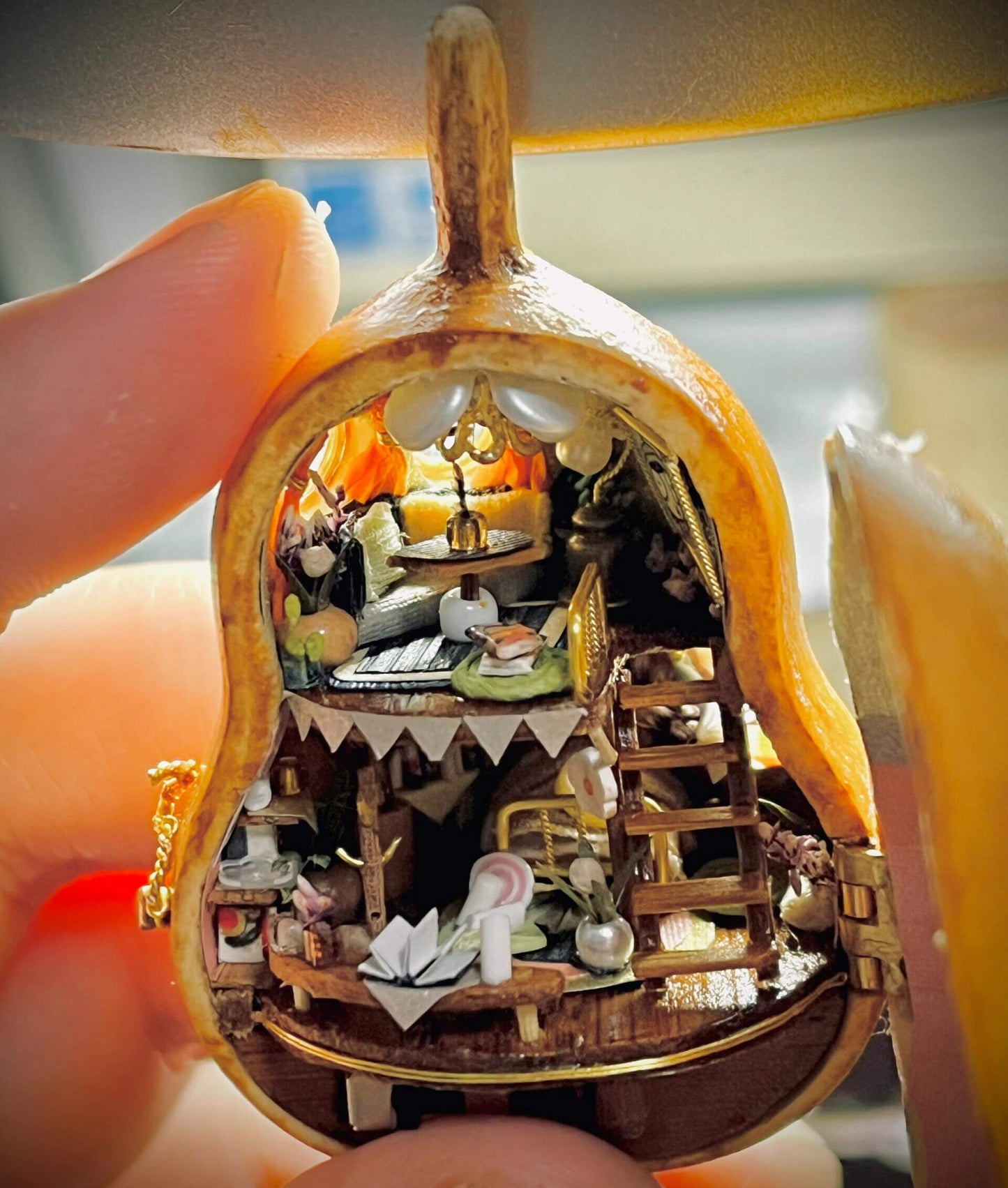 This intricate diorama captures a magical miniature home inside a gourd. The multi-level design showcases a cozy bedroom, a charming dining setup, and whimsical decorations. Adorned with delicate bunting, flowers, books, and candles, every detail exudes warmth and creativity. This enchanting craft is a tiny masterpiece that feels alive with stories waiting to unfold.