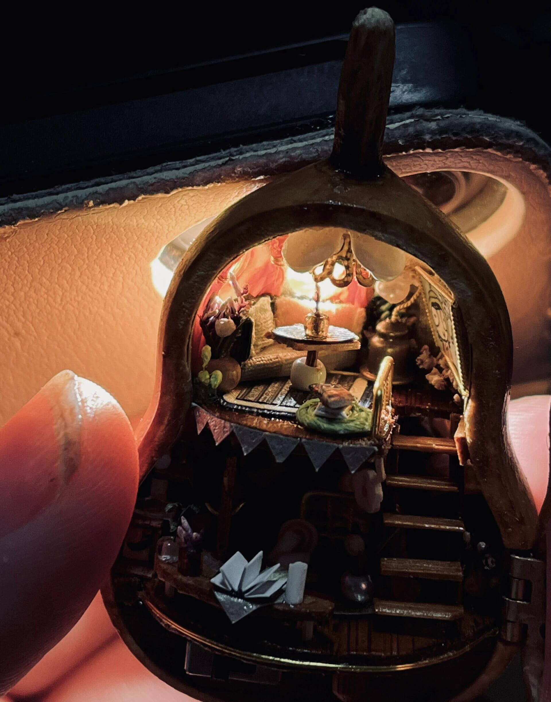 This intricate diorama captures a magical miniature home inside a gourd. The multi-level design showcases a cozy bedroom, a charming dining setup, and whimsical decorations. Adorned with delicate bunting, flowers, books, and candles, every detail exudes warmth and creativity. This enchanting craft is a tiny masterpiece that feels alive with stories waiting to unfold.