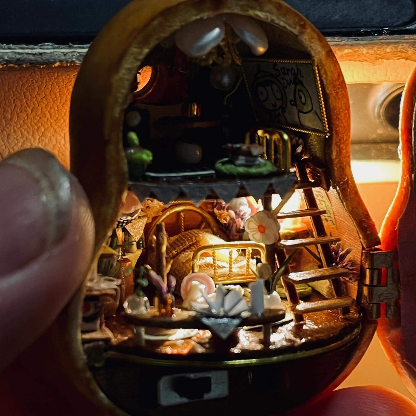 This intricate diorama captures a magical miniature home inside a gourd. The multi-level design showcases a cozy bedroom, a charming dining setup, and whimsical decorations. Adorned with delicate bunting, flowers, books, and candles, every detail exudes warmth and creativity. This enchanting craft is a tiny masterpiece that feels alive with stories waiting to unfold.