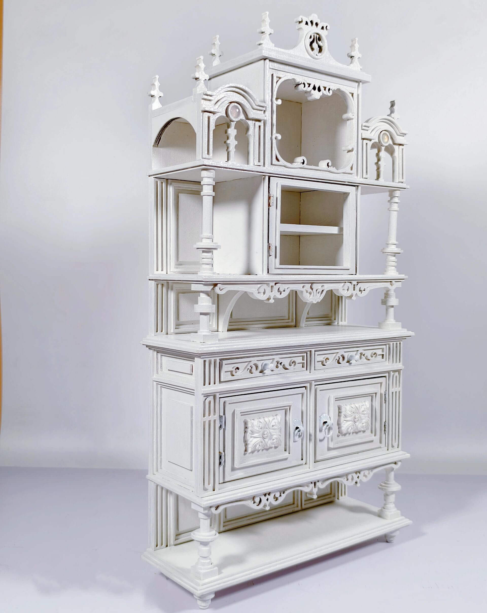 Enhance your dollhouse dining area with this Miniature Antique Buffet Cabinet with Carved and Shelves Kit. This beautifully crafted buffet features both open shelves for displaying miniatures and closed compartments for storage, all adorned with intricately carved decorative details and an elegant design. Available in various sizes, this buffet is perfect for showcasing fine dining accessories, storing dishes, or adding a sophisticated, vintage touch to your miniature kitchen or dining room.