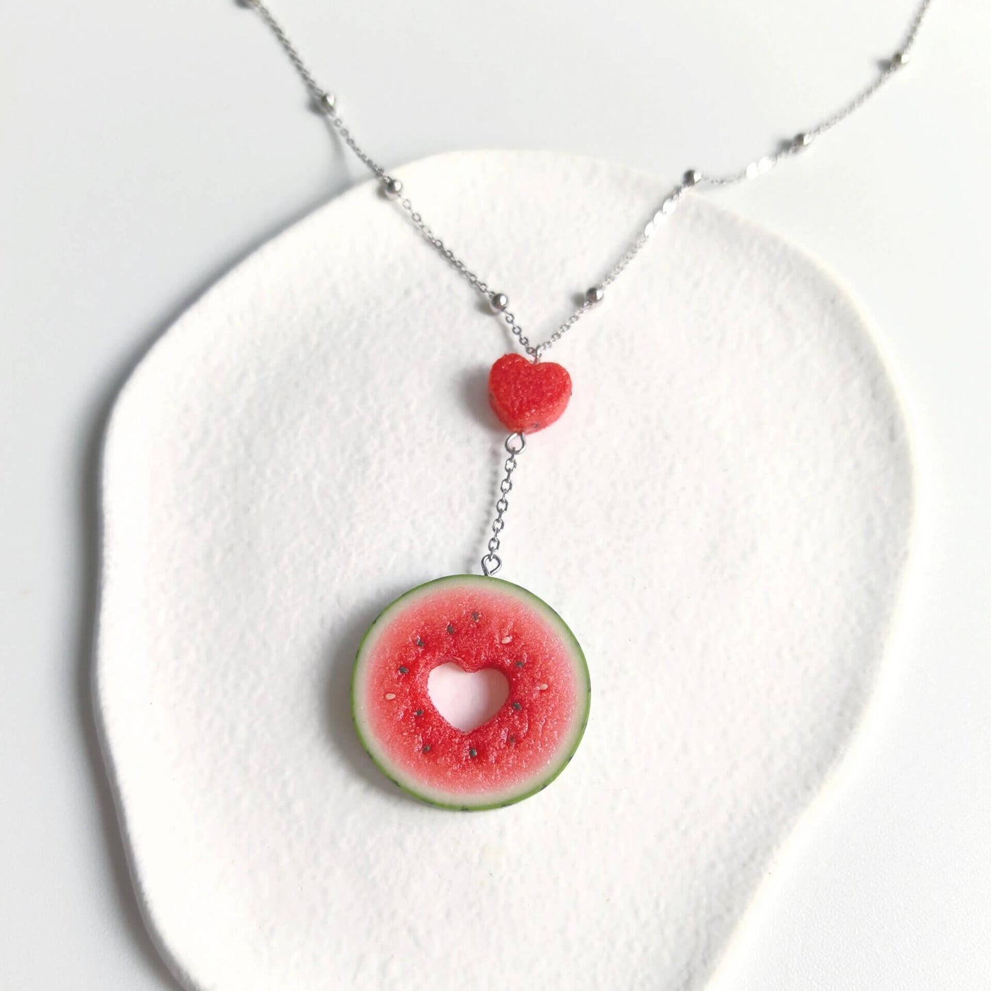 Cute realistic round watermelon slice with cut in the shape of heart necklace with sterling silver chain. The watermelon are made with polymer clay and then finished with a gloss varnish. The necklace are made from high-quality materials and are durable, but should not be put in aggressive environments like excessive moisture, chemicals or perfume.